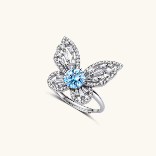 Sterling silver ring with blue moissanite center stone surrounded by clear stones in butterfly wing pattern on white background