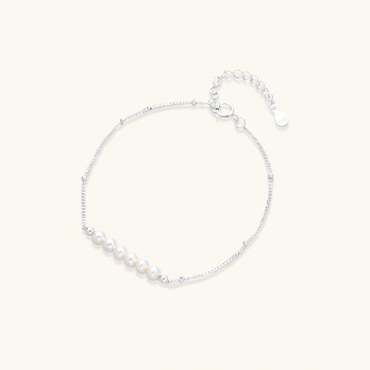 Delicate rhodium-plated silver chain bracelet with row of small baroque pearls centered on white background.